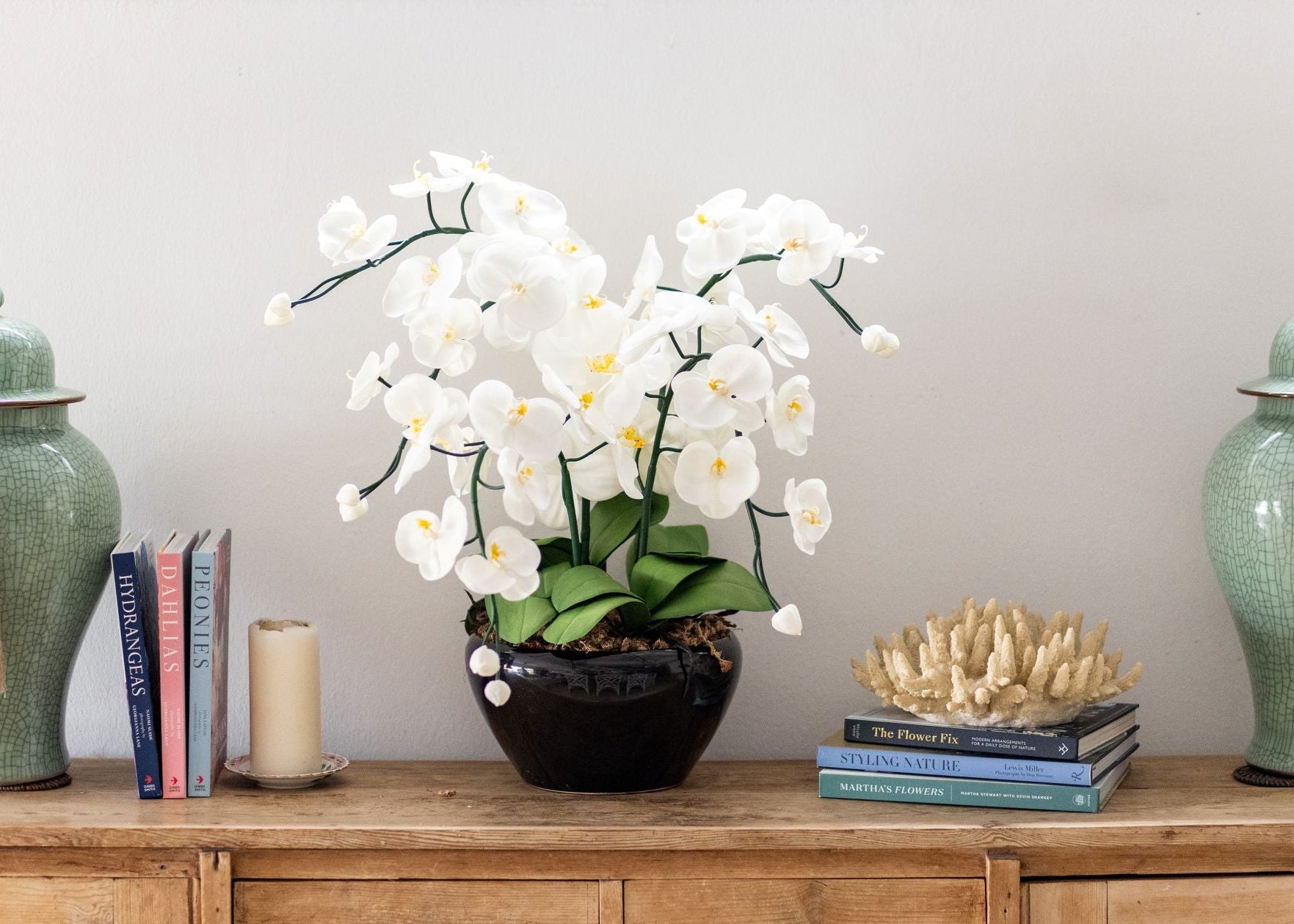 Large artificial orchid on wooden sideboard with decorative items including vases