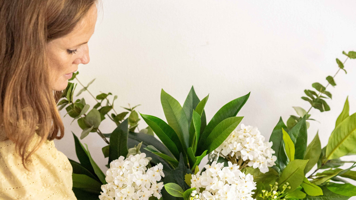Woman arranging flowers in a vase on a table with a white background
